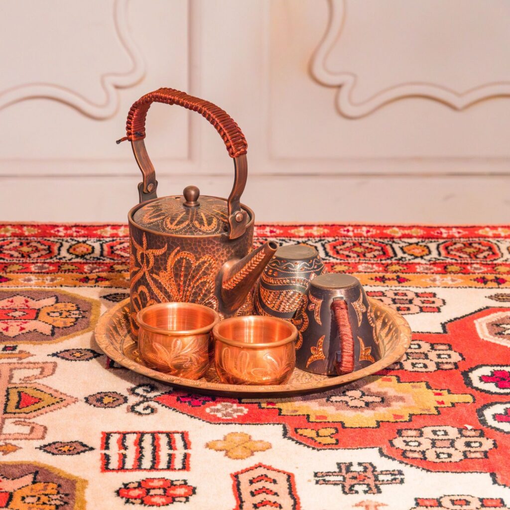 An ornate, engraved copper tea set displayed on a vibrant, traditional patterned rug.